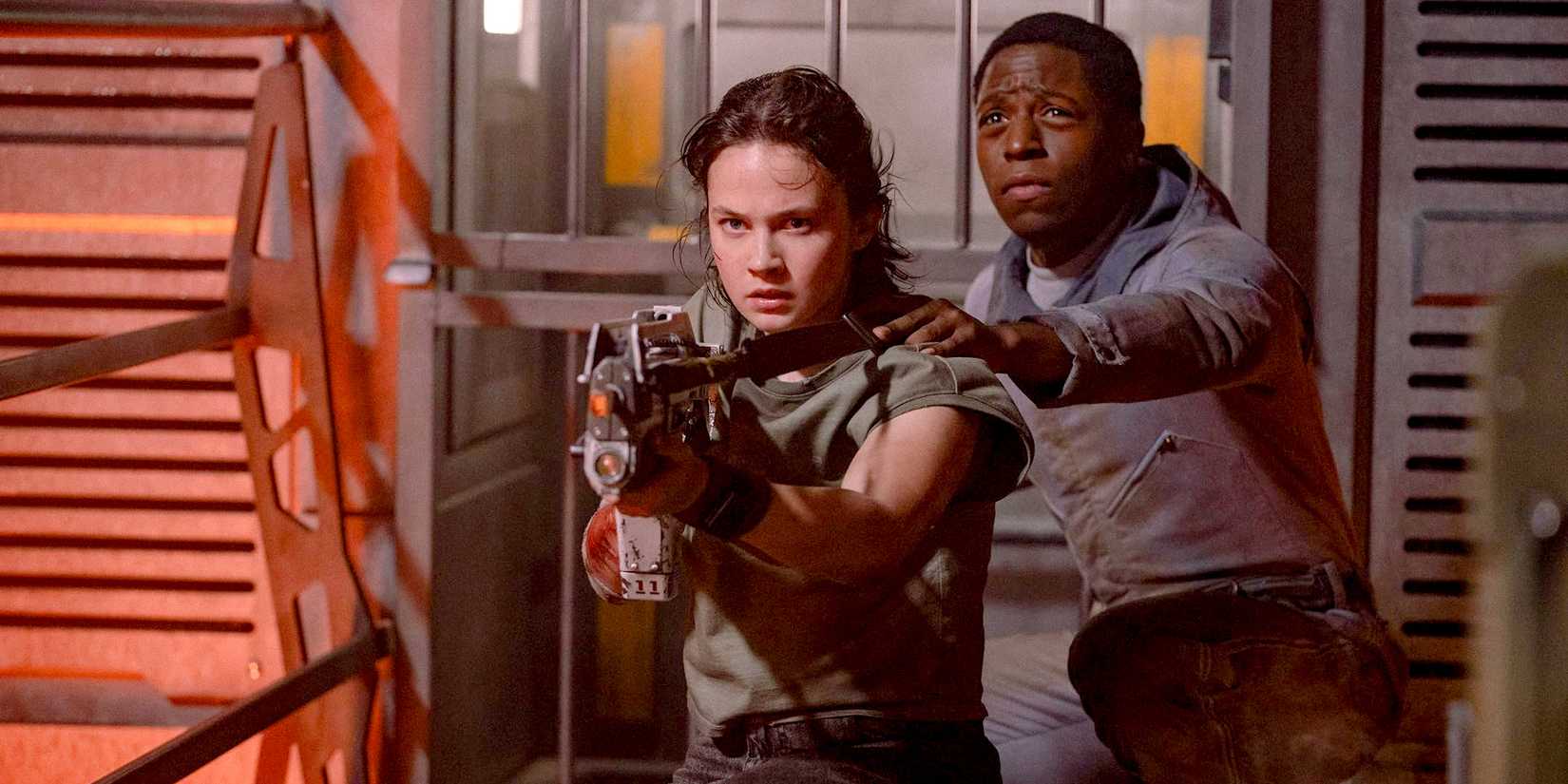 Rain (Cailee Spaeny) pointing a gun while Andy (David Jonsson) stands behind her in Alien: Romulus
