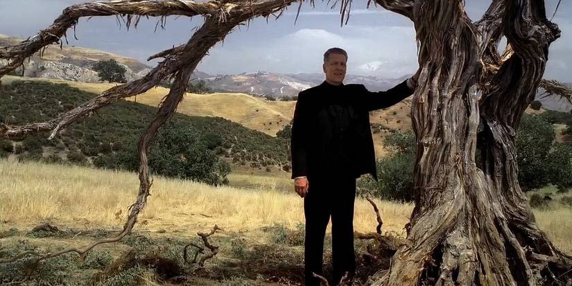 Brother Justin (Clancy Brown) si appoggia su un albero nodoso in Carnivàle
