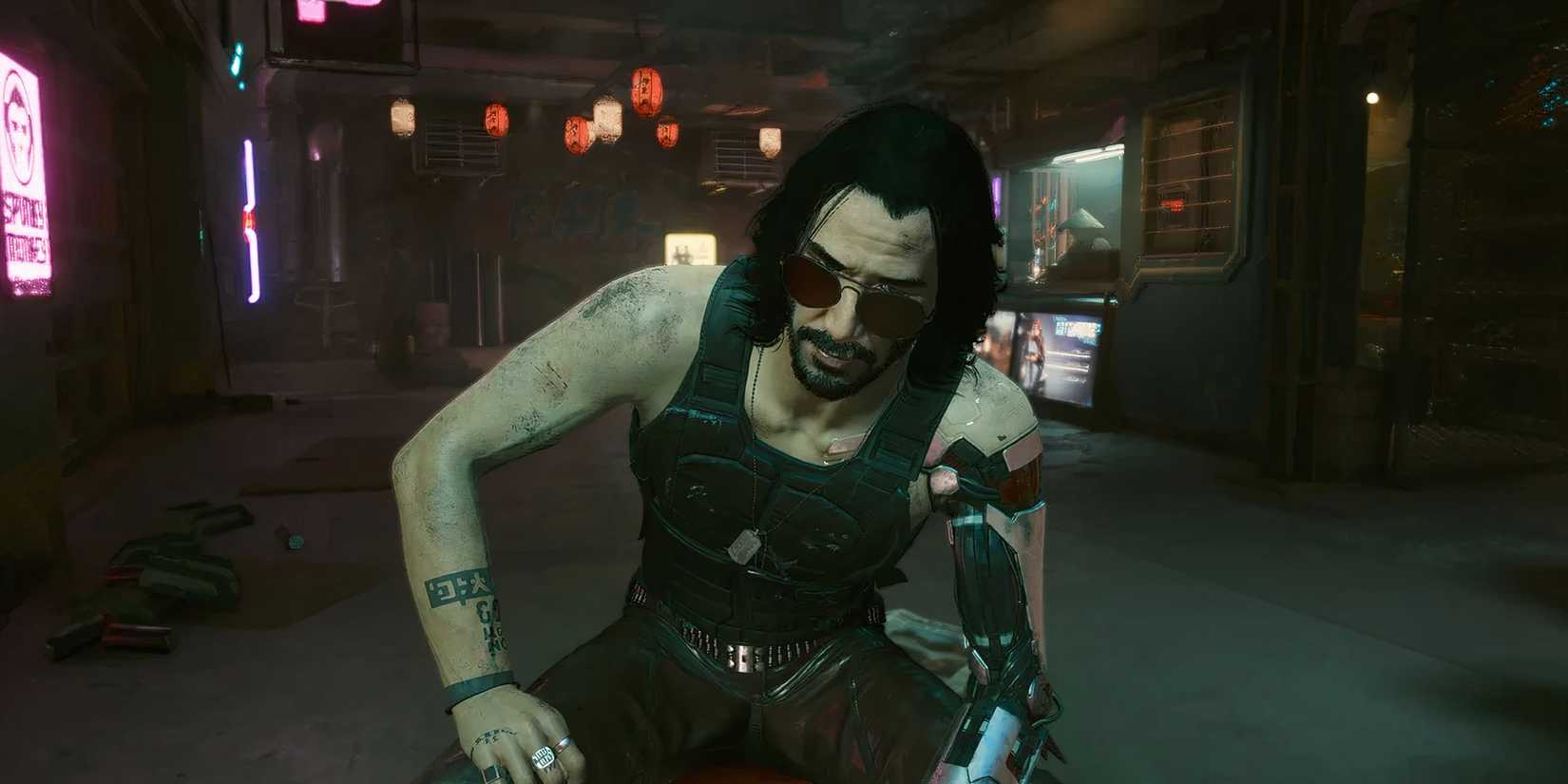 Johnny sat on a chair looking at V from behind his sunglasses in Cyberpunk 2077.