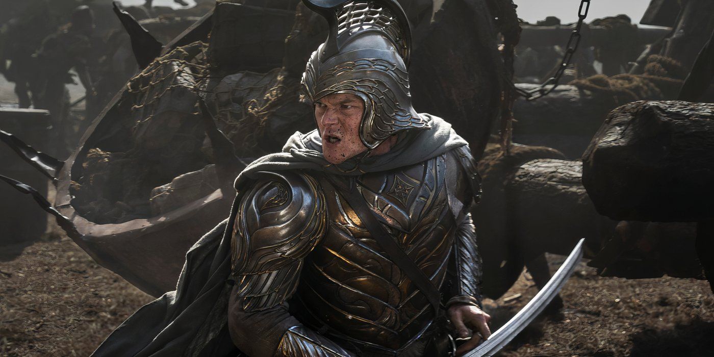 Elrond clad in armor standing in the middle of a battle with mud on his face and a sword in his hand in Rings of Power season 2