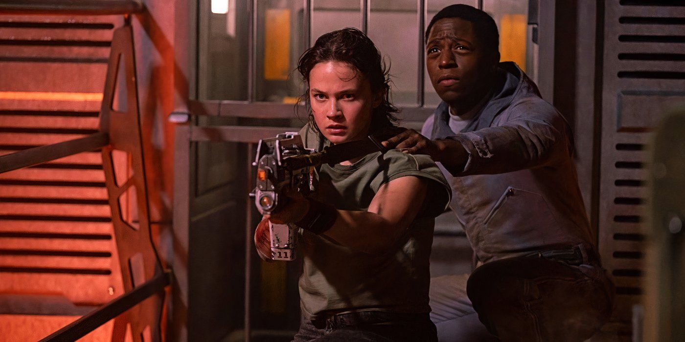 Cailee Spaeny as Rain points a gun while Andy stands behind her in Alien: Romulus