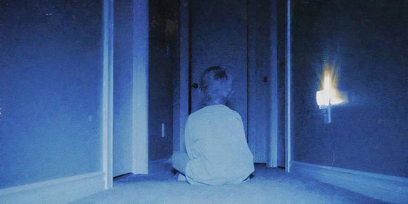 A kid sits in a dark hallway in Skinamarink