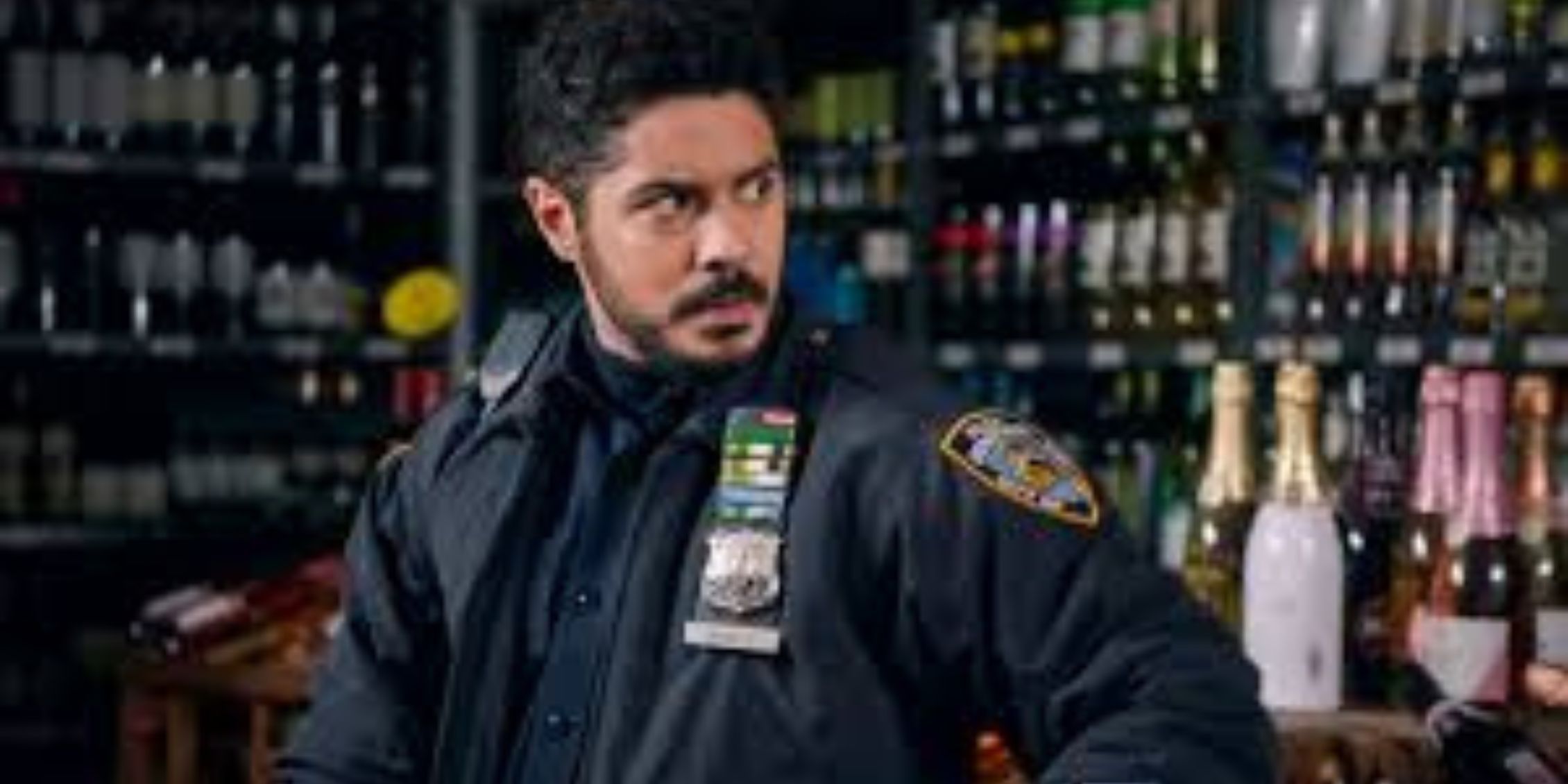 Blue Bloods Badillo standing in a liquor store in uniform with his hands on his hips