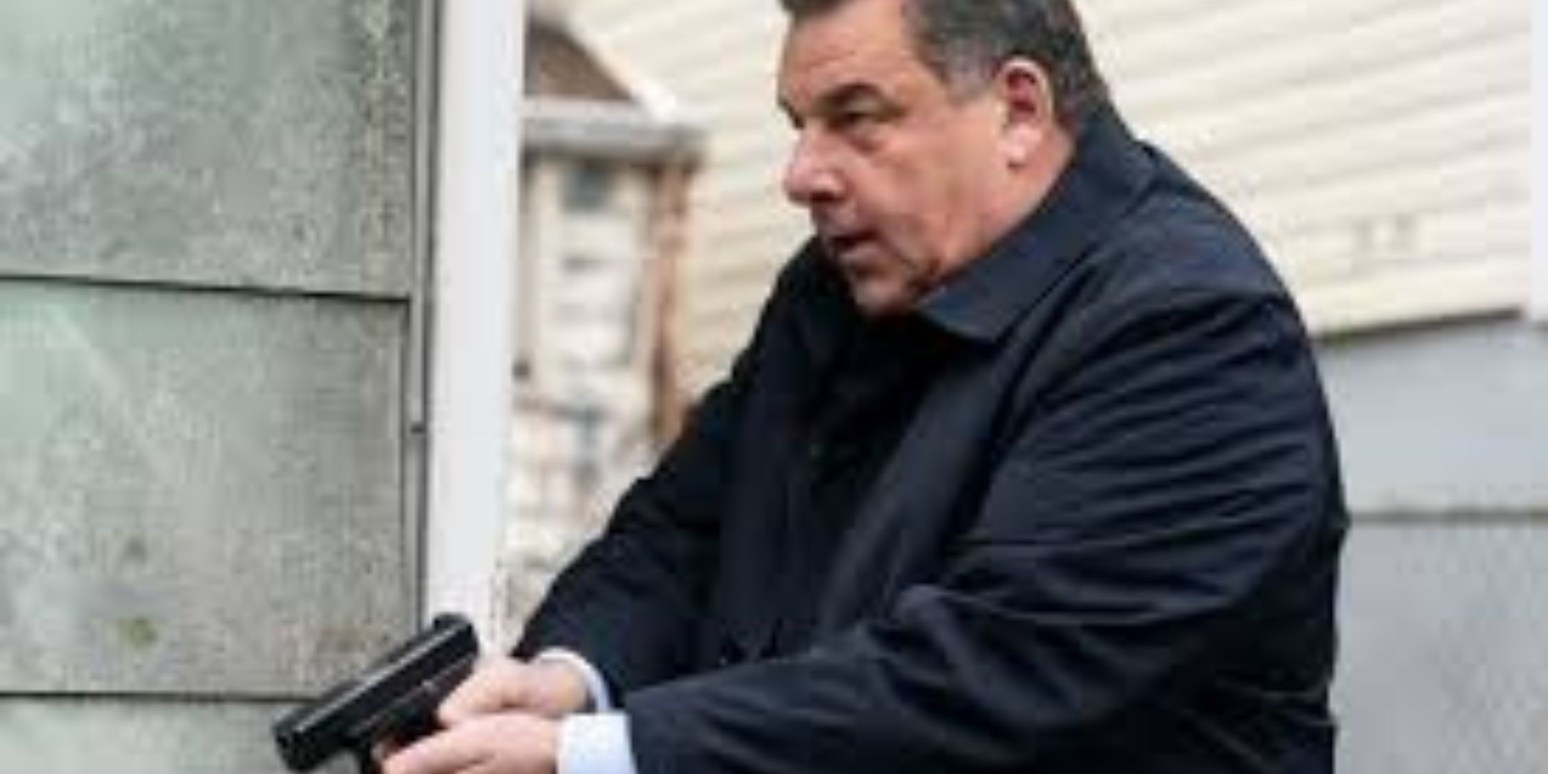 Blue Bloods Anthony stands at the corner of a house holding his gun out