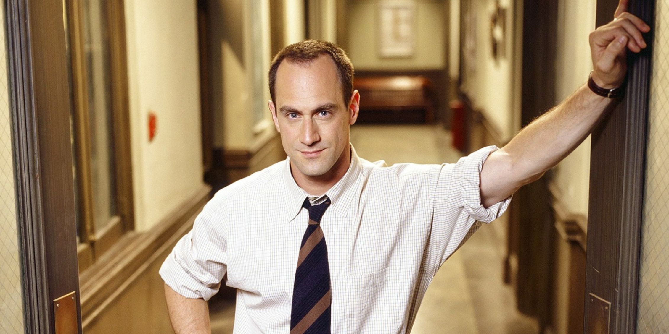 Law & Order: SVU Stabler stands in a hallway with one hand on his hip looking confident