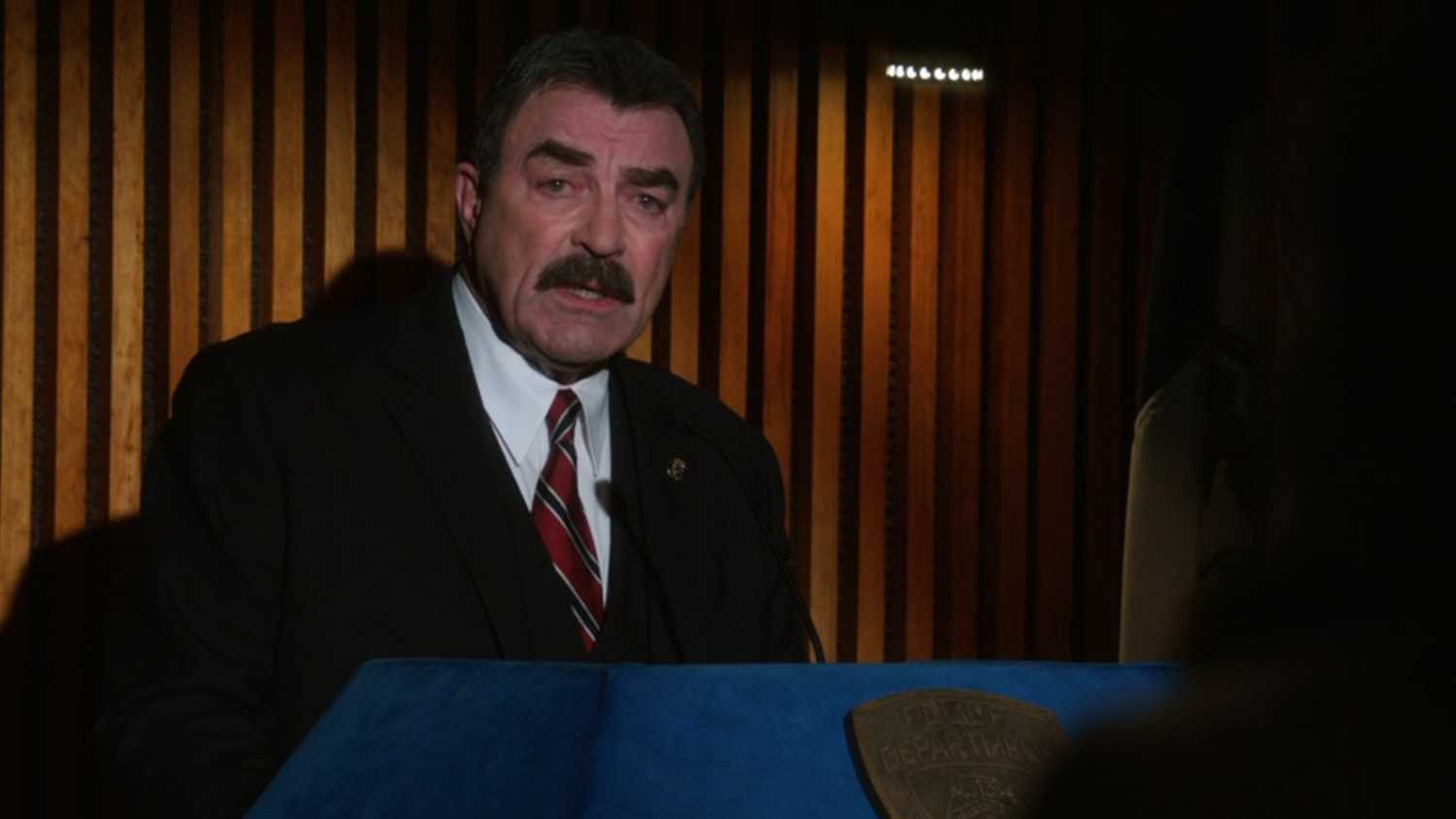 Blue Bloods with Frank behind a podium with his glasses off
