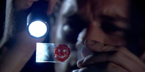 Dexter Morgan (Michael C. Hall) looking at a blood slide with a smiley face in it in Dexter season 1, episode 6