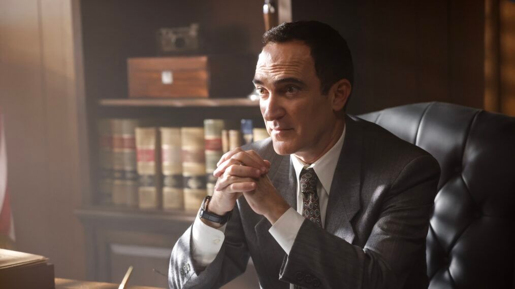 Cliff Walker (Patrick Fischler) sits behind a desk with his hands clasped in front of him in NCIS Origins