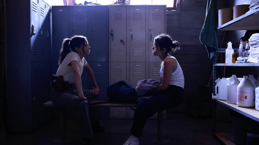Lala and Vera sit opposite each other on a bench in the locker room in NCIS Origins