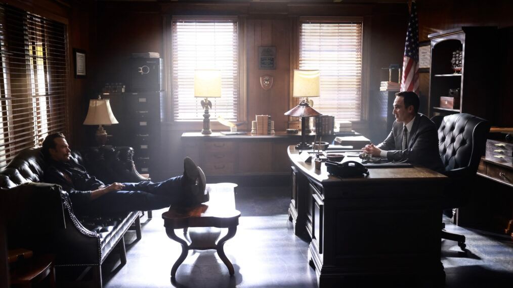Mike Franks sits on a couch across the room from Cliff Walker, who sits behind a desk, in NCIS Origins