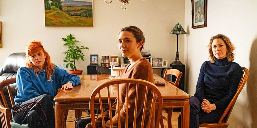 natasha lyonna elizabeth olsen and carrie coon sit at a kitchen table and look toward the camera in his three daughters