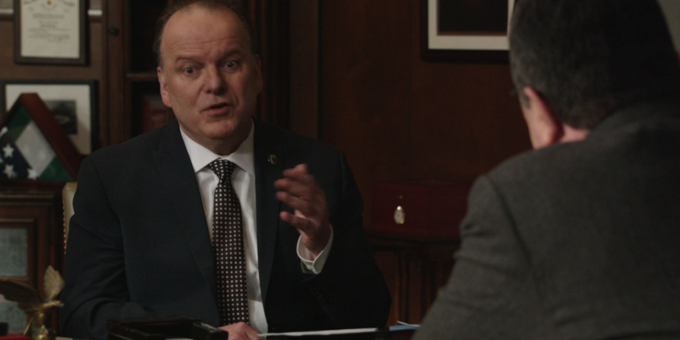 Sid holds his hand up while making a point in a discussion with Frank on Blue Bloods