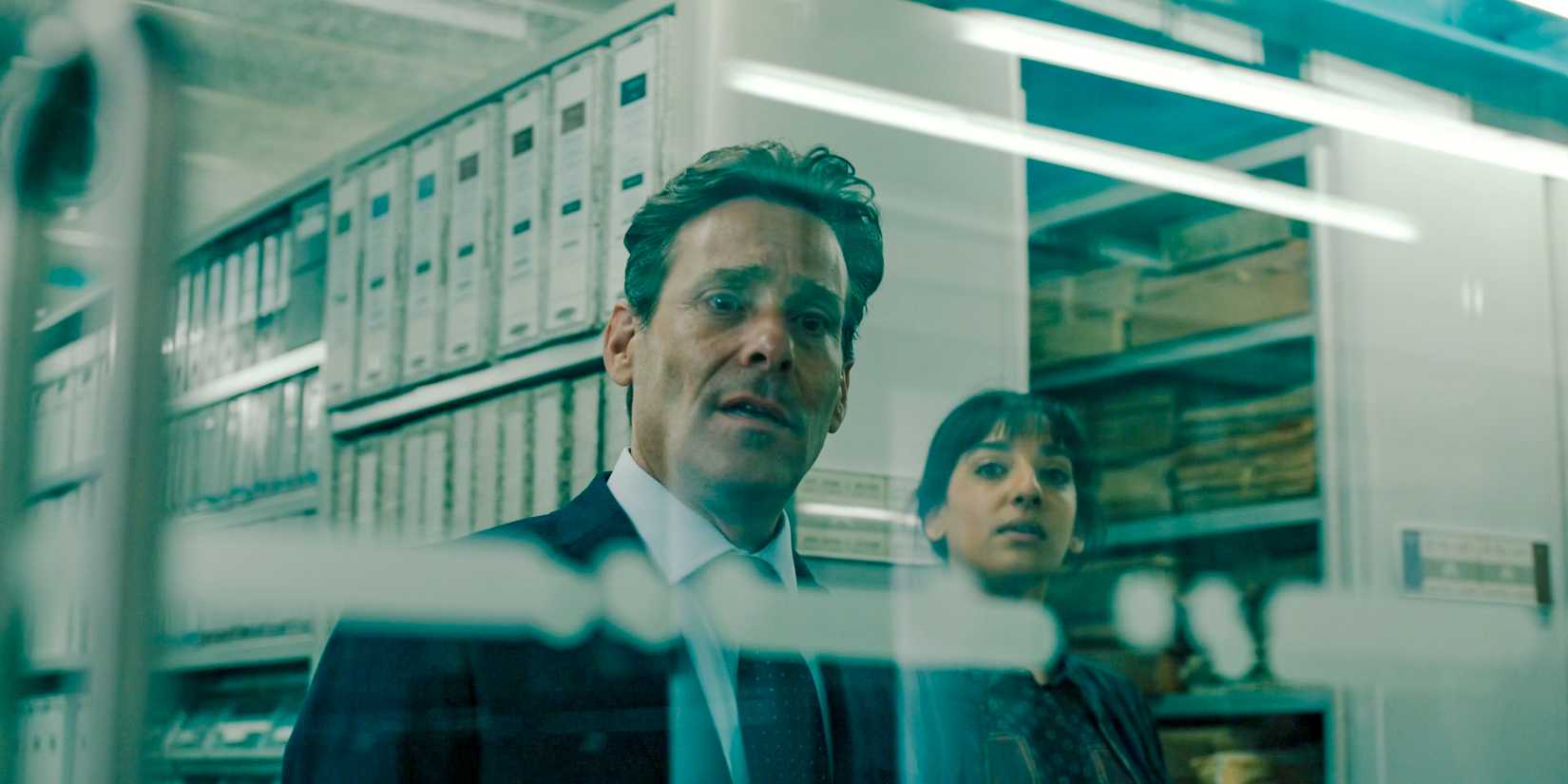 Claude Whelan (James Callis) and Giti (Kiran Sonia Sawar) looking through a window in Slow Horses Season 4 Episode 3