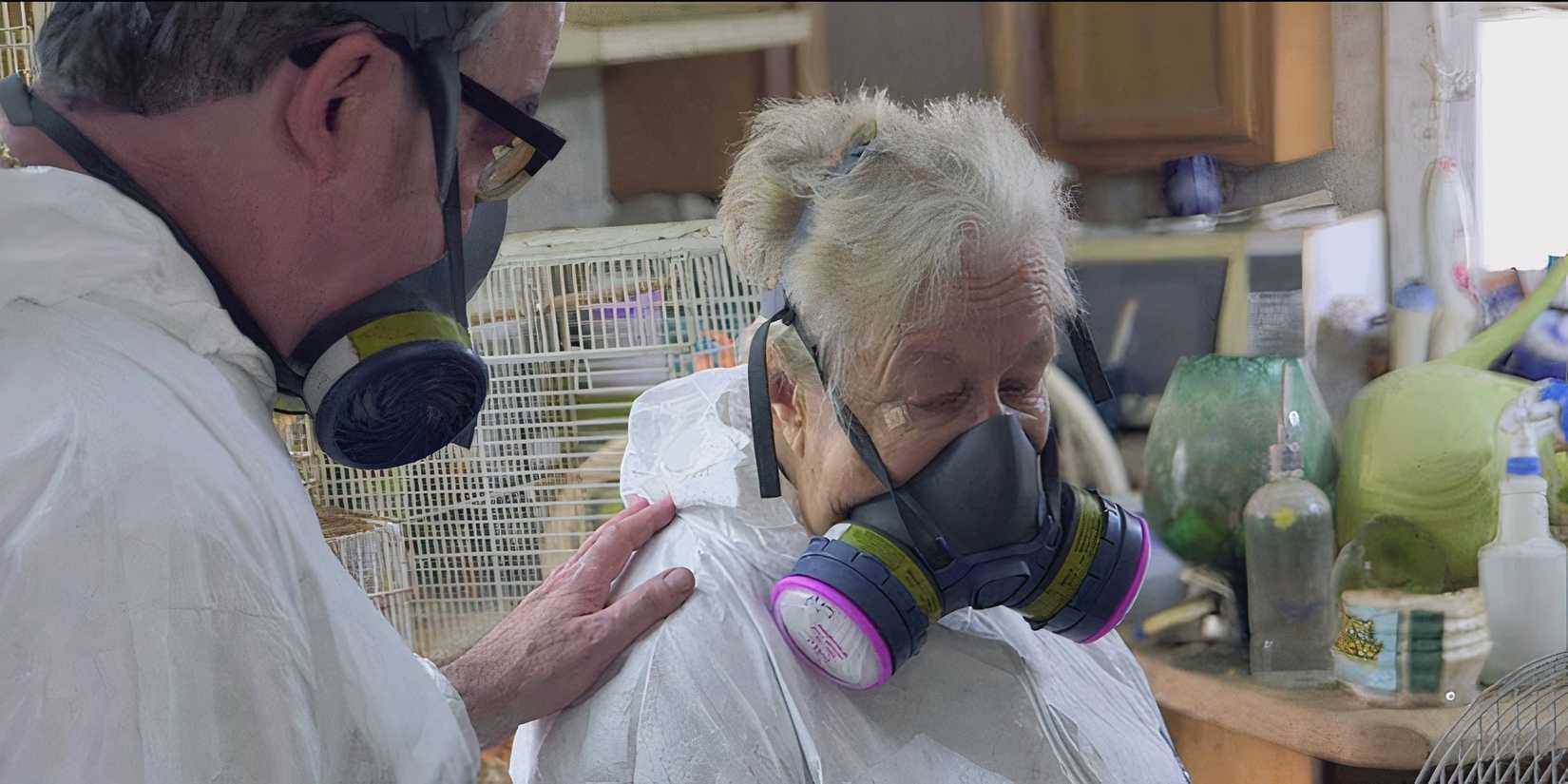 Two people in masks while working in a room full of clutter and animal cages in Hoarders season 8 episode 8