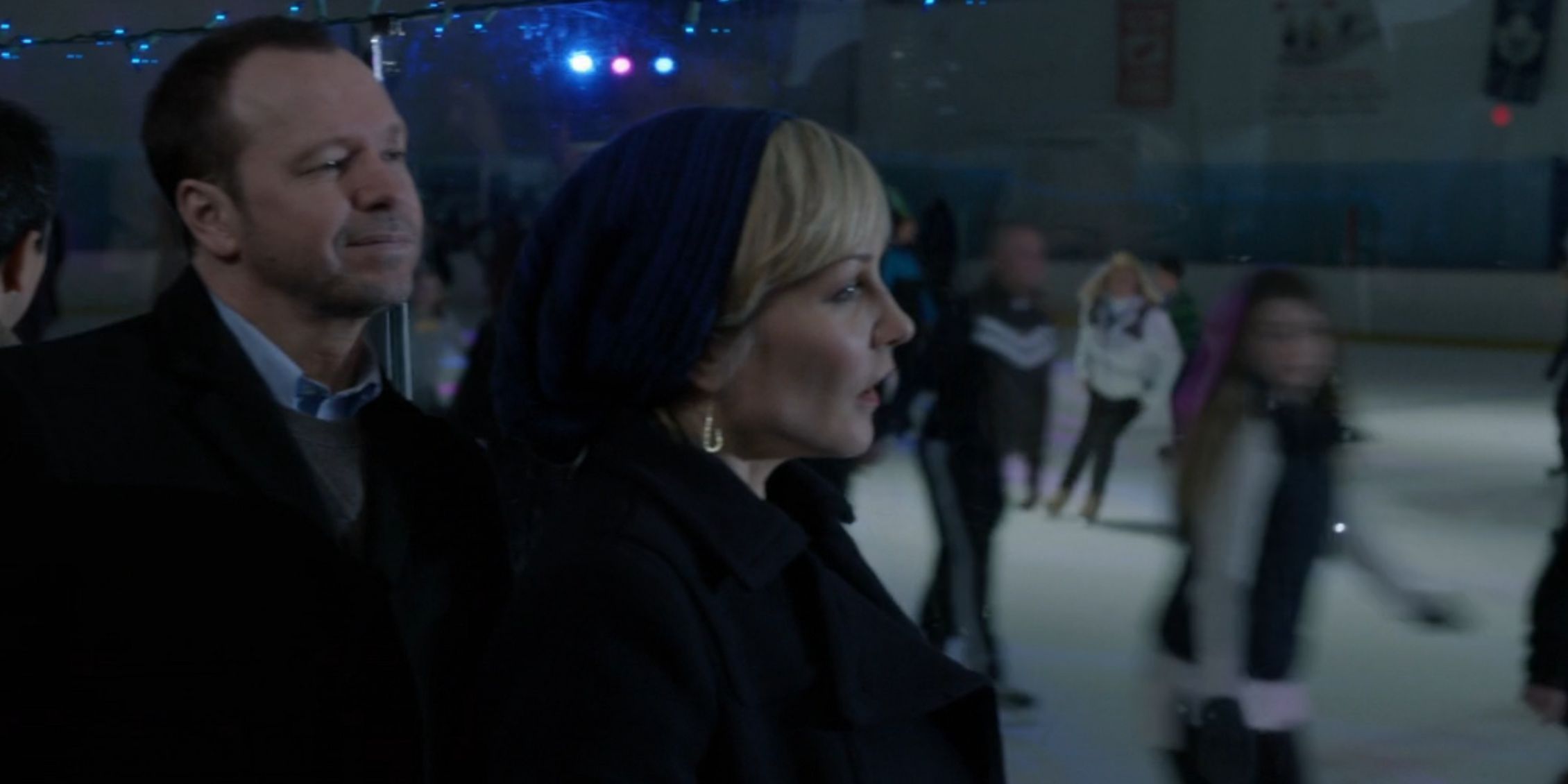 Blue Bloods Linda wearing a coat and Danny standing behind her watching the kids skate