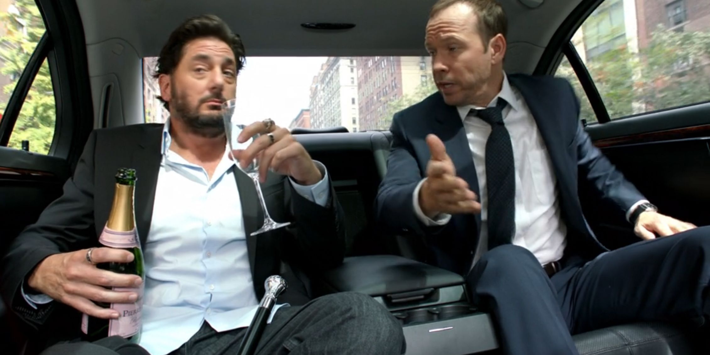 Danny in the back seat of a limo with a man who is drinking alcohol in Blue Bloods