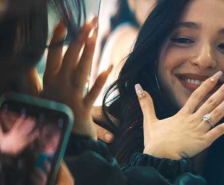 Anora смотрит в зеркало, рассматривая свой свадебный кольцо и улыбается в Anora