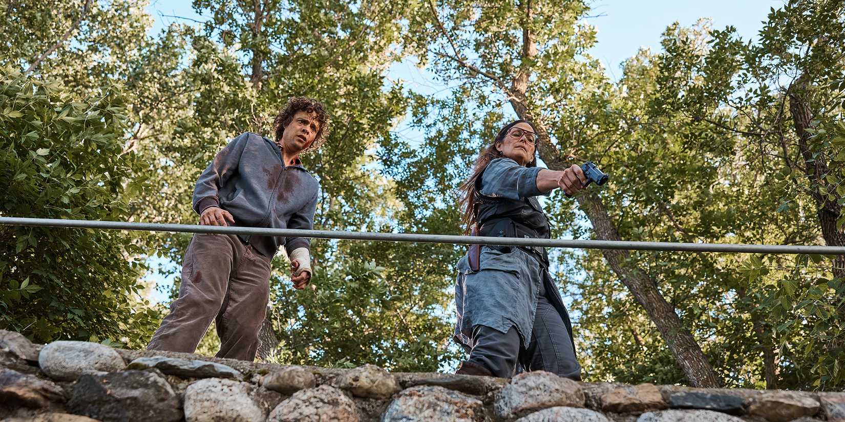 Douglas Smith's Ethan looking scared standing next to Carrie-Anne Moss' Mae aiming a gun in Die Alone