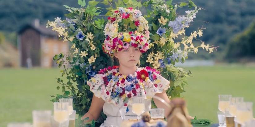Dani (Florence Pugh) wears a flower crown and necklace while sitting in a flowery chair in Midsommar