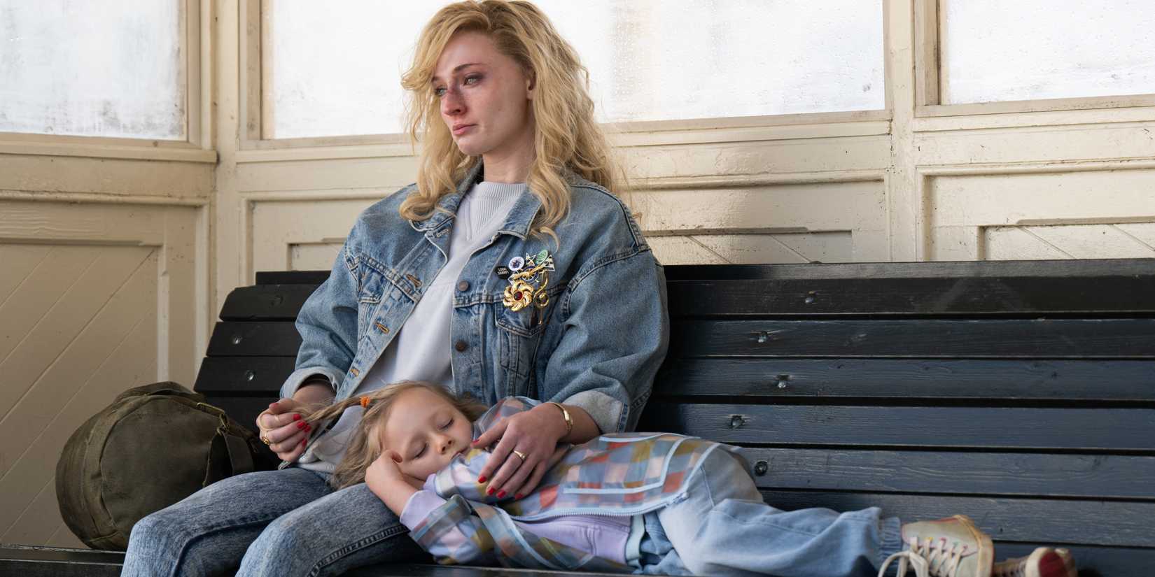 Sophie Turner As Joan Hannington & Mia Millichamp-Long As Kelly laying on a train bench In The CW's Joan, Season 1, Episode 1.