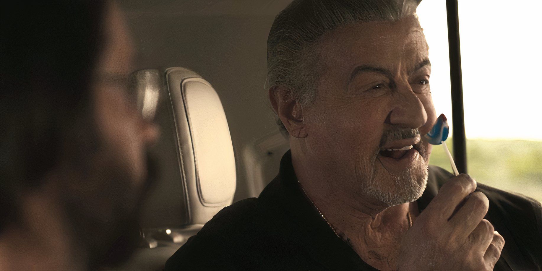 Dwight Manfredi (Sylvester Stallone) holding a lollipop and laughing in Tulsa King season 2, episode 4