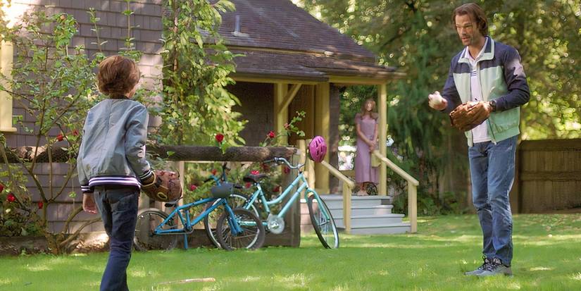 Sam Winchester playing catch with his son as a woman watches in Supernatural.