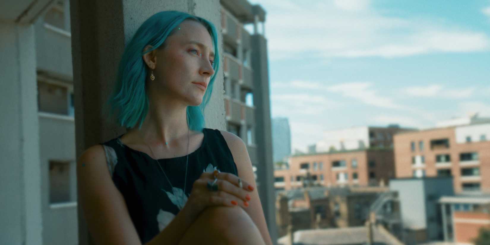 Saoirse Ronan smokes a cigarette while looking out a window in The Outrun