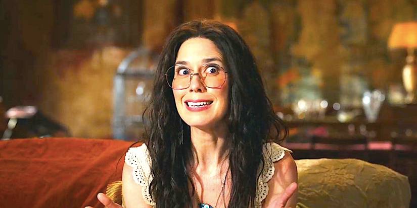 Sheila Carrasco's Flower sits on a couch smiling in Ghosts season 4 episode 1