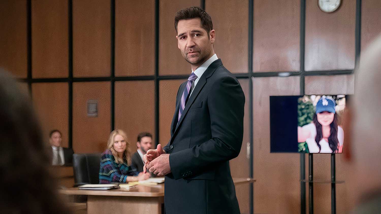 Mickey stands in the courtroom with a picture of Glory Days in the background in The Lincoln Lawyer season 3 episode 6
