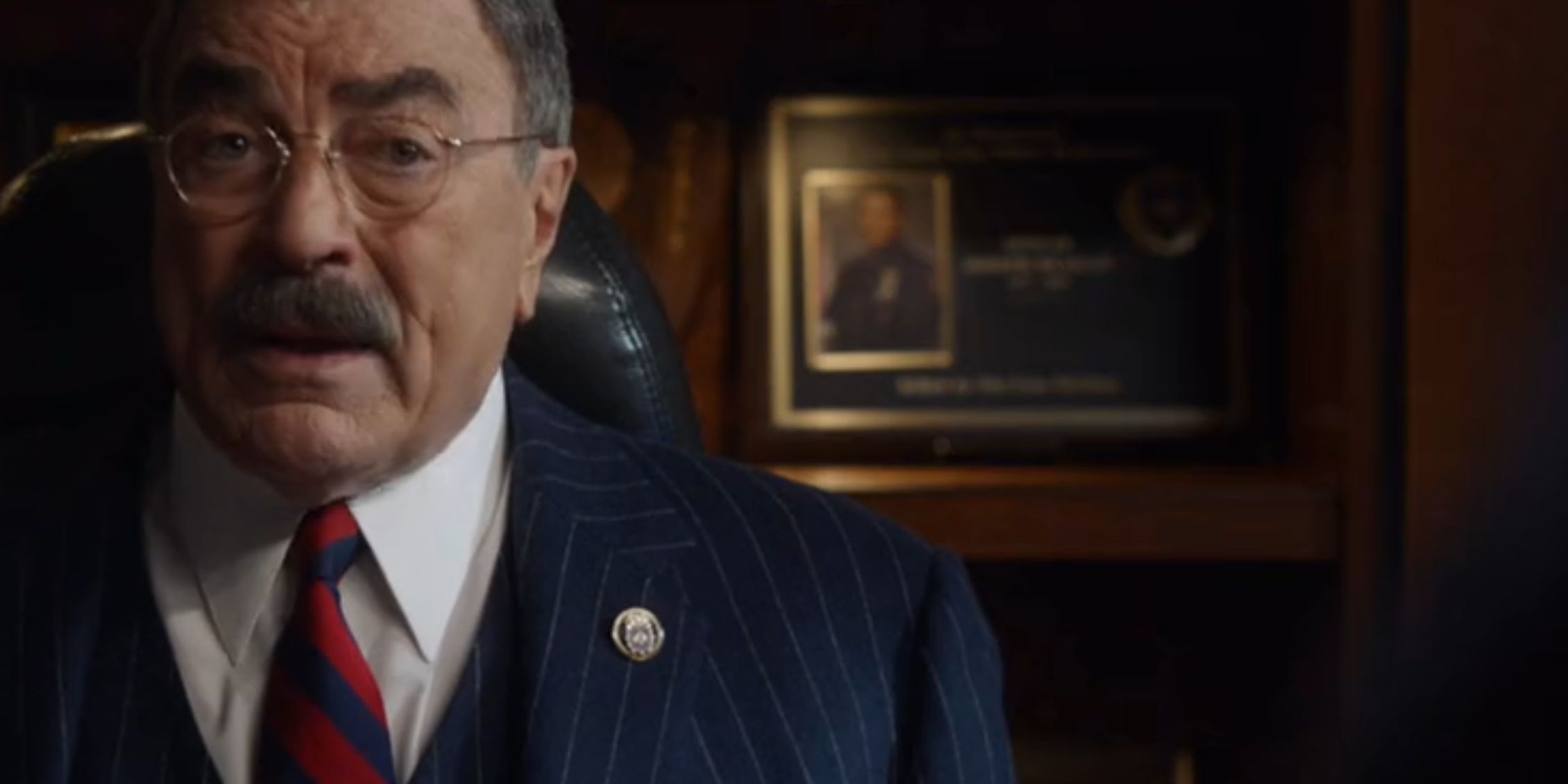 Frank sitting behind his desk looking serious while talking