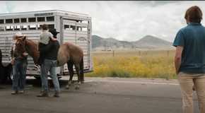Yellowstone Rip taking a child over to a horse by a caravan