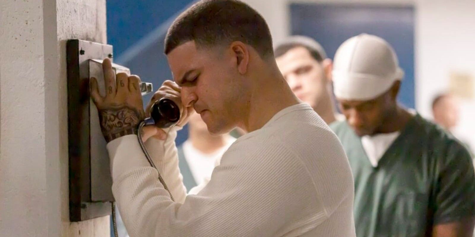 Aaron Hernandez holding a phone in prison, looking devastated, in American Sports Story