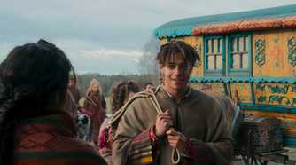 Aram stands in front of a colorful Tuatha'an wagon in The Wheel of Time