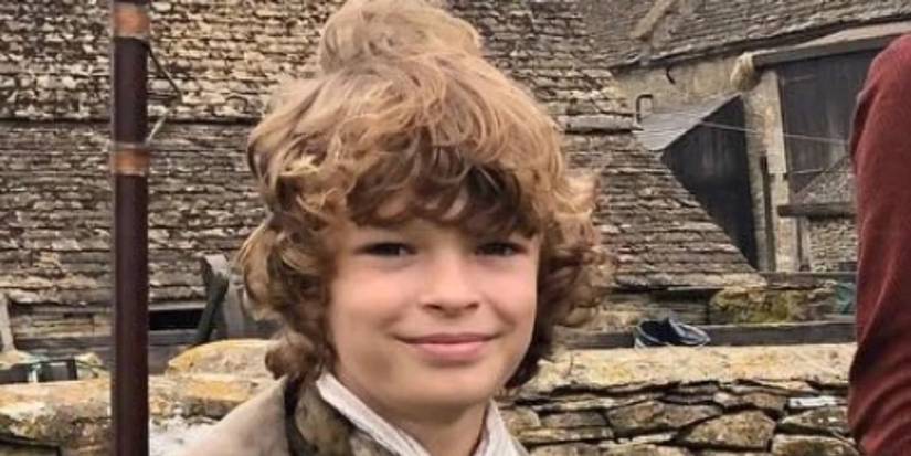 Jeremy Poldark (Oscar Novak) holding a rifle and smiling in Poldark