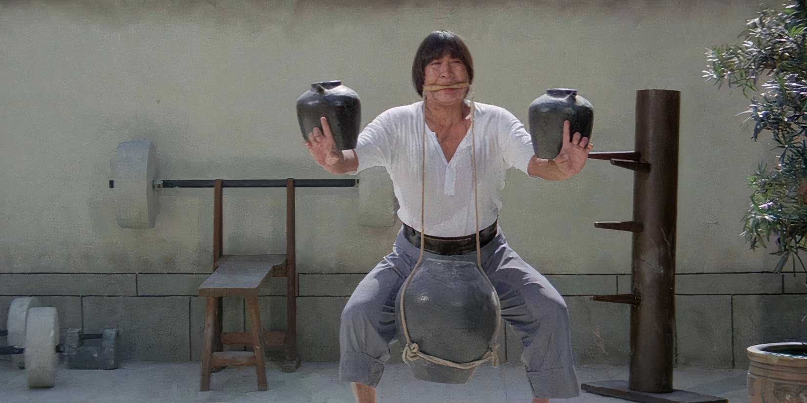 Sammo Hung struggles to hold a heavy object up by a rope in his mouth. 