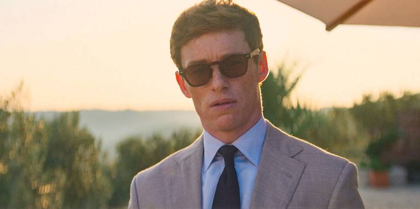 Eddie Redmayne como The Jackal com uma expressão incerta, vestindo terno e óculos escuros em The Day of the Jackal