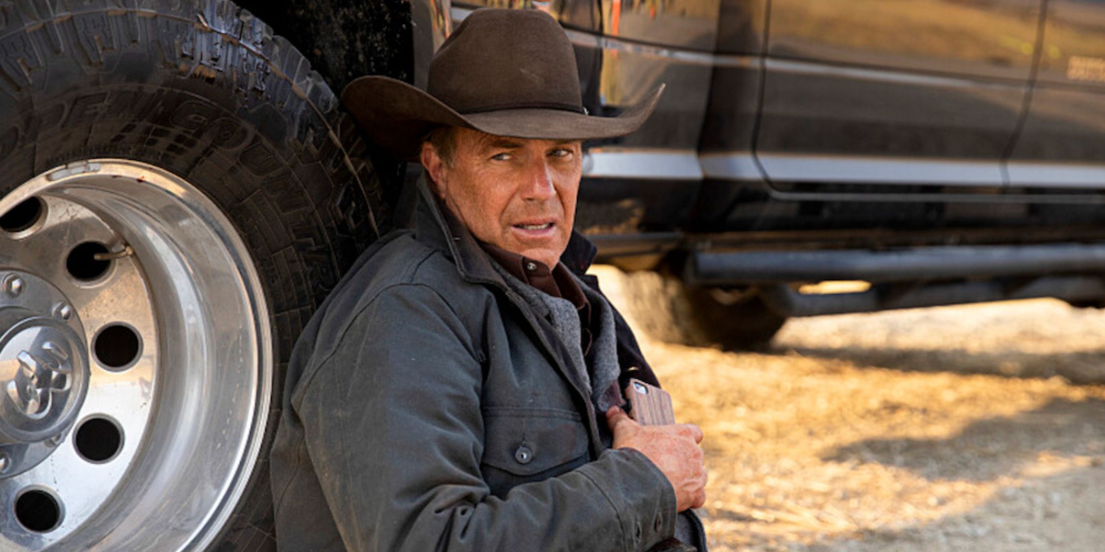 Yellowstone John Dutton sitting by his jeep holding his side after getting shot