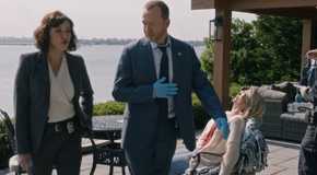 Blue Bloods Danny And Baez wearing blue gloves while a dead body sits behind them in a deck chair