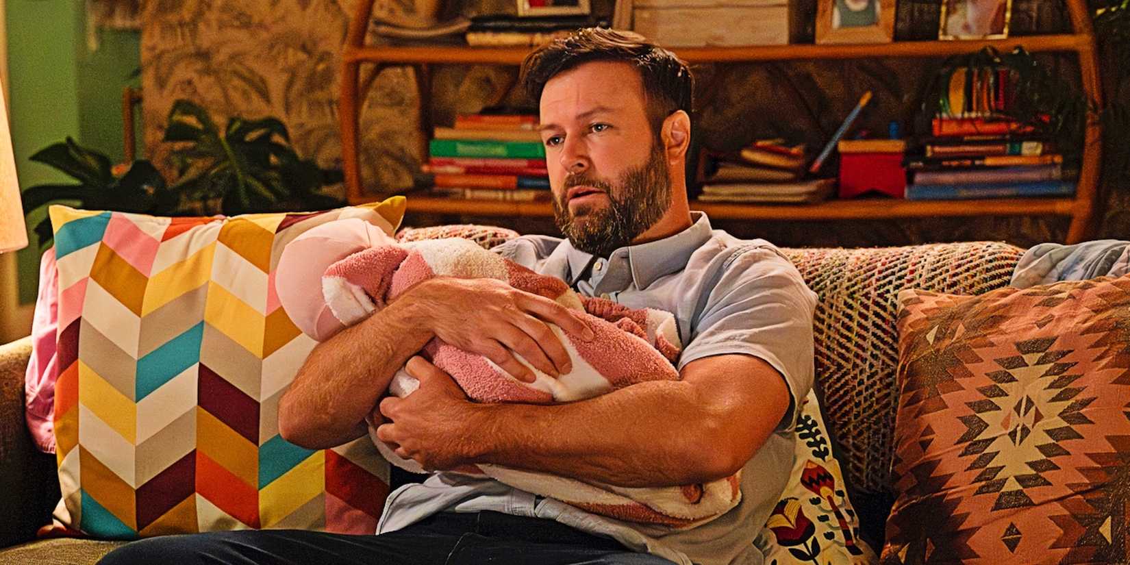 Taran Killam as Ludo Radovic holding a baby in "High Potential."