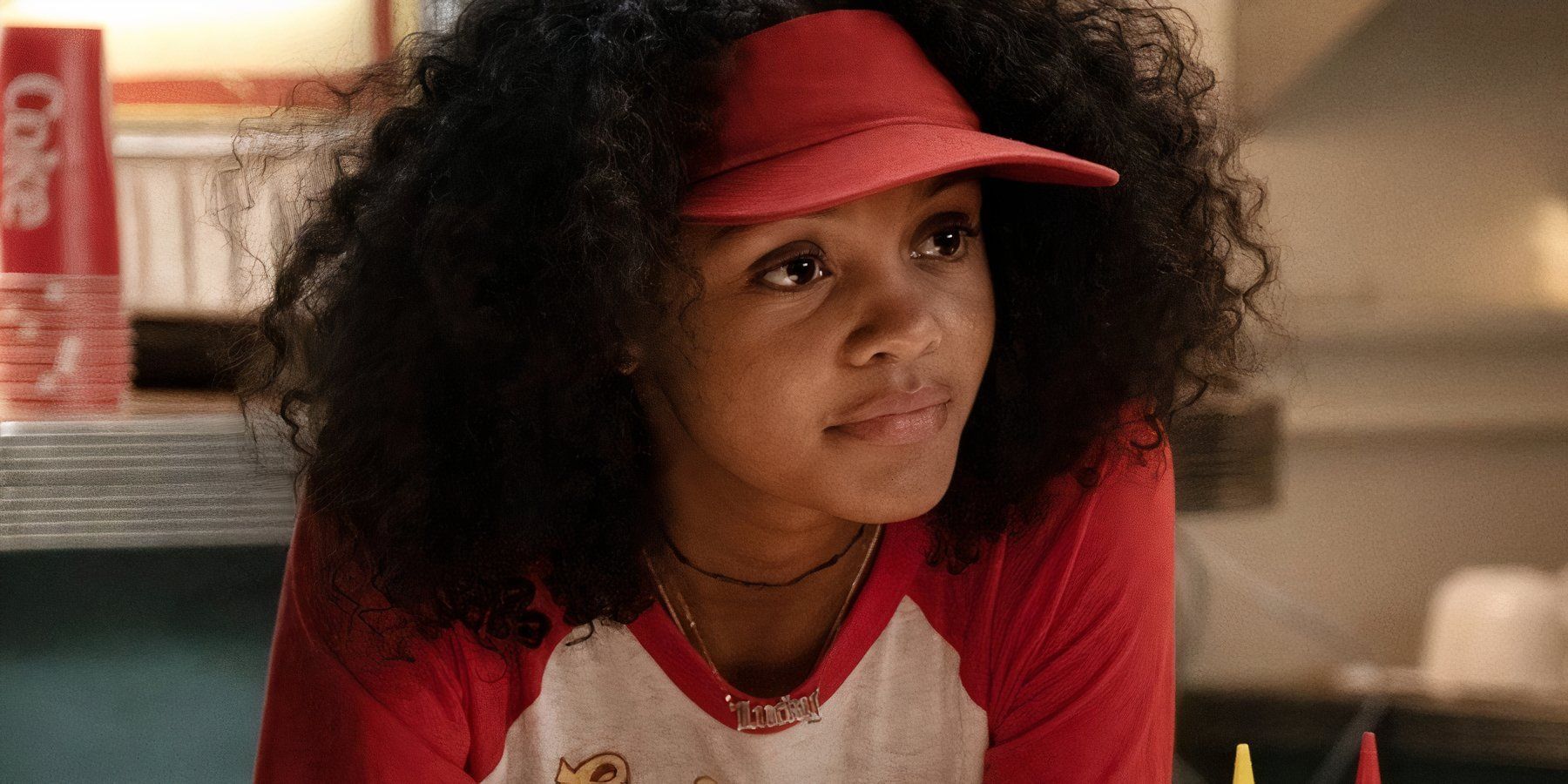 Celeste O&rsquo;Connor as Lucky Domingo in her red burger joint employee uniform and visor in Ghostbusters: Afterlife