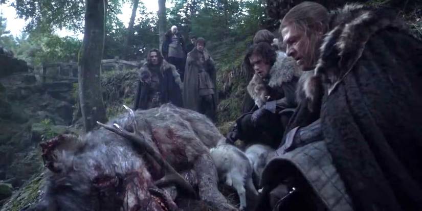 Ned Stark e Jon Snow ajoelhados sobre um lobo gigante morto com chifres em seu interior no episódio piloto de Game of Thrones