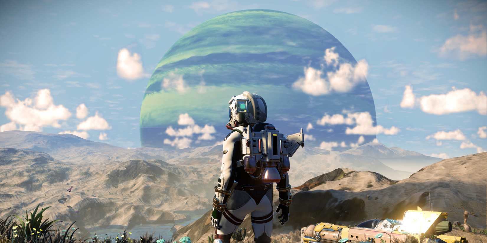 A player character in a spacesuit standing on a small ridge, overlooking his neighboring ship and a large striped planet on the horizon, in a screenshot from the No Man's Sky Worlds Part 2 update.