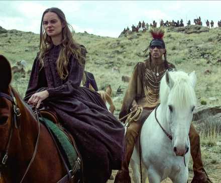 A woman rides beside a Native American man
