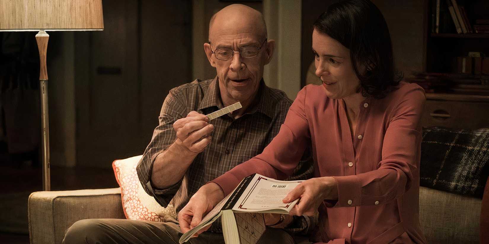 J.K. Simmons and Olivia Williams sit together on a couch and examine a piece of paper.