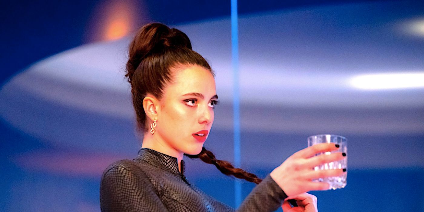 Margaret Qualley como Sue em The Substance, brindando com um copo de whisky.