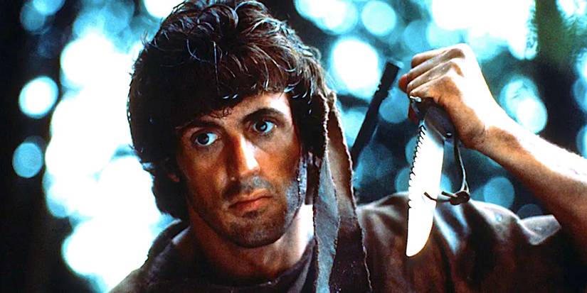 Sylvester Stallone como John Rambo encara enquanto segura uma faca de caça em Rambo: Programado para Matar 1982