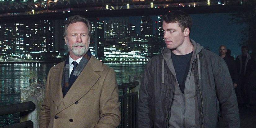 Louis Herthum (Jacob Monroe) e Gabriel Basso (Peter Sutherland) caminhando com a cidade ao fundo em The Night Agent