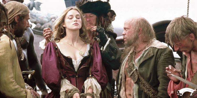 Keira Knightley as Elizabeth Swann being held hostage by pirates and wearing a red dress in Pirates of the Caribbean: The Curse of the Black Pearl.