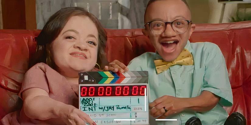 Джей и Памела, держа в руках реквизит, улыбаются, сидя на диване.