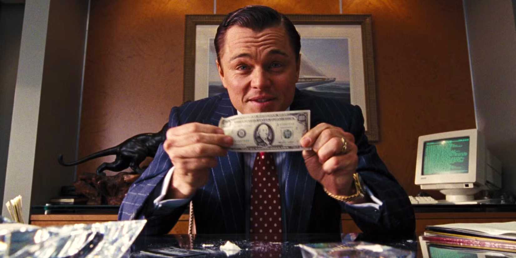 Leonardo DiCaprio holding up a 100 dollar bill to camera in The Wolf of Wall Street
